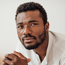 Young black man with beard gazes into camera with hands clasped.