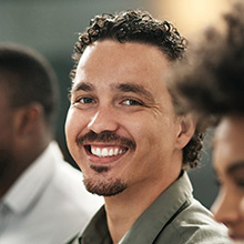 Latino man sitting among a crowd smiles.