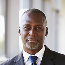 Black man in business suit smiles in his office.