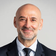 White man in open button-up shirt smiles in his office.